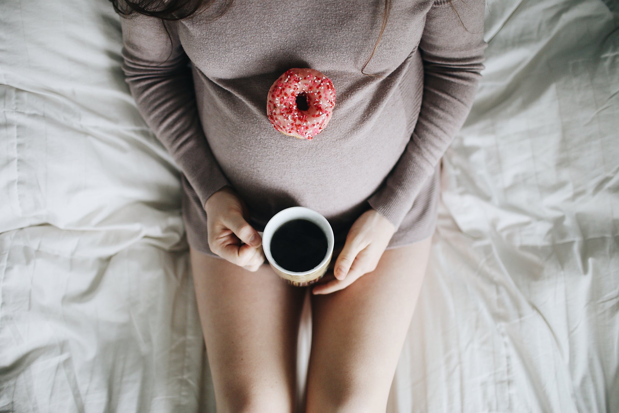 Pregnant woman resting with a coffee with a doughnut on her baby bump