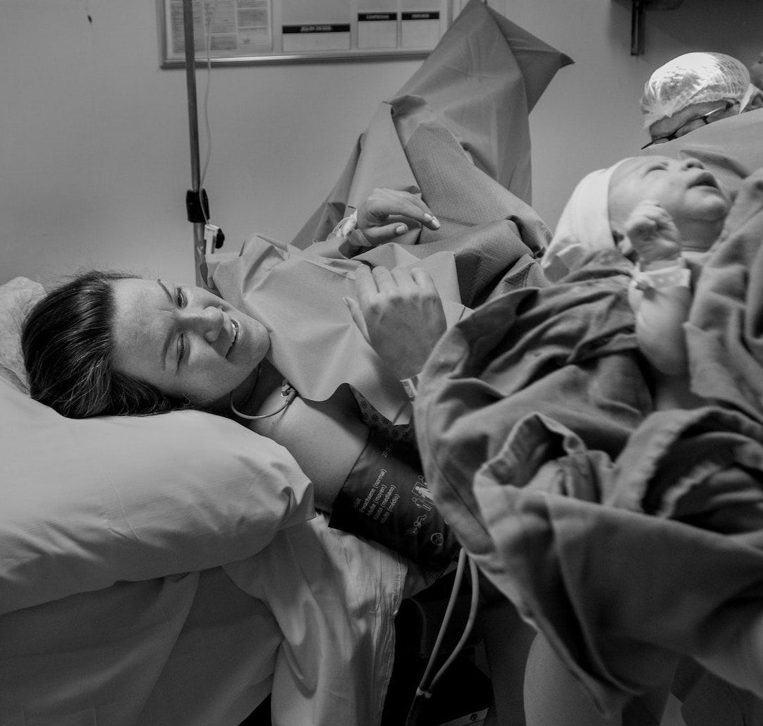 Black and white photo of smiling woman having positive c-section and being shown her baby