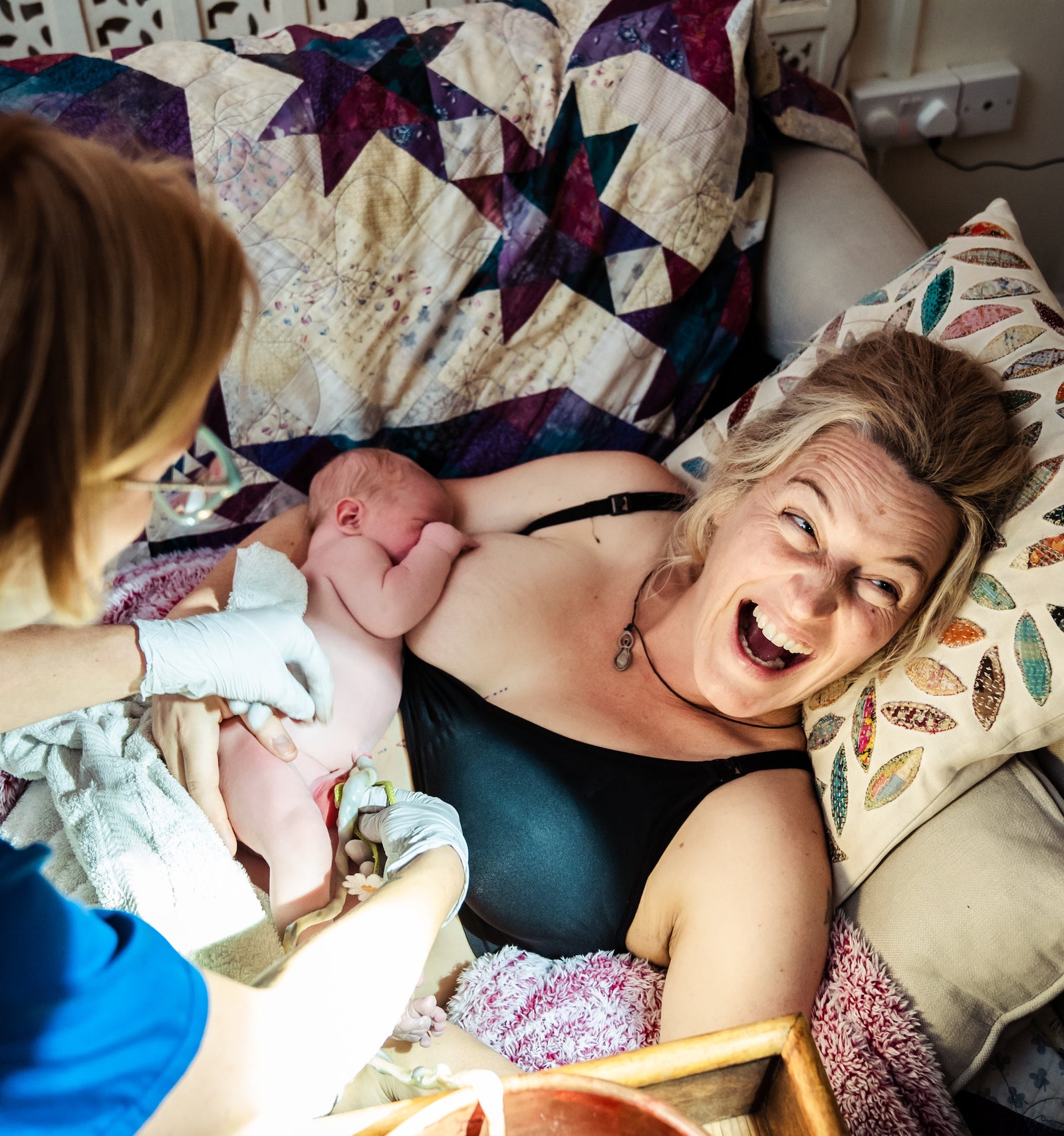 Woman laughing after birth whilst breastfeeding newborn baby